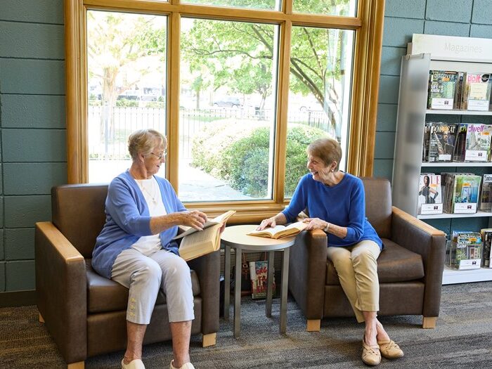 Two women sitting in chairs by the window talking and reading