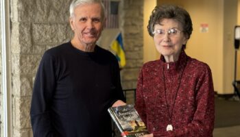 Library volunteer hands library book to senior woman who uses Library's homebound delivery service.