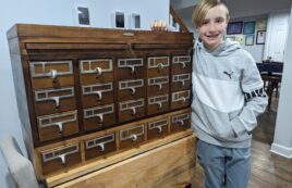 Scout Owen Hanba poses with the antique library card catalog he refurbished to be used to store the seed library collection.