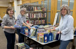Three female volunteers arrange and sort books for the annual book sale fundraiser.