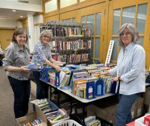 Three female volunteers arrange and sort books for the annual book sale fundraiser.