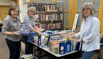 Three female volunteers arrange and sort books for the annual book sale fundraiser.