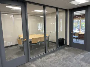 Glass-walled room with blonde-wood table and chairs for six people showing study space option in library.