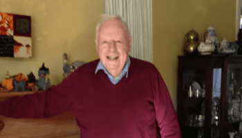 A photo of Dave Donovan standing next to his fireplace in a red sweater.